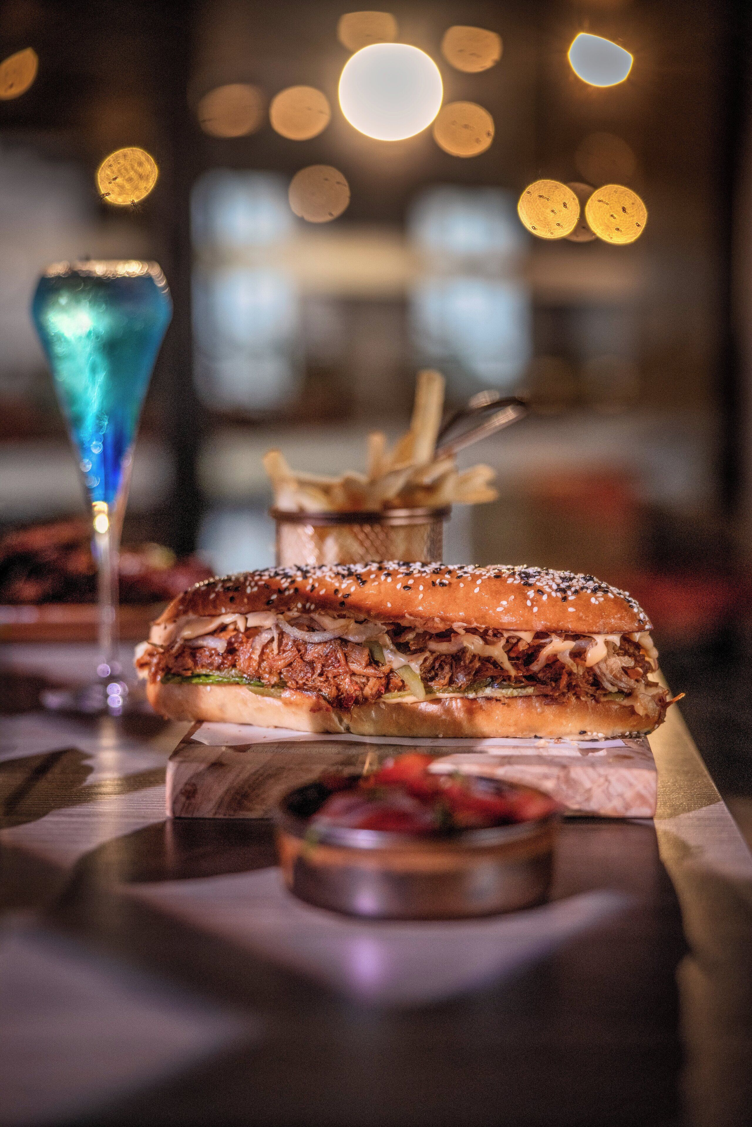 A restaurant setting with a pulled pork sandwich, fries, and a blue drink on a wooden table.