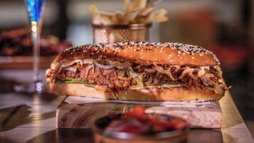 A restaurant setting with a pulled pork sandwich, fries, and a blue drink on a wooden table.