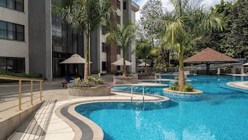 Un hotel moderno con una amplia piscina exterior rodeada de palmeras y jardineras.