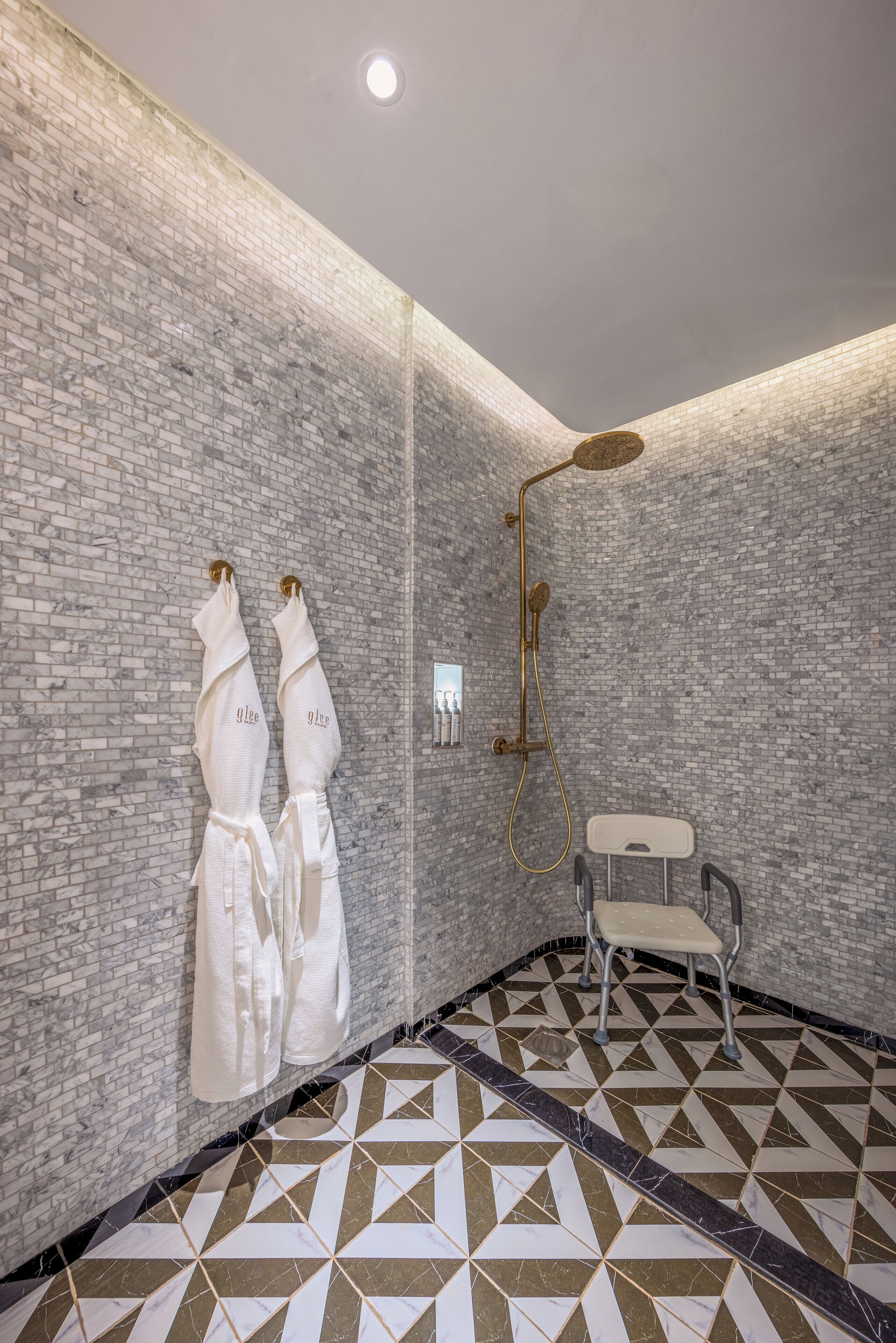 A modern bathroom with a brick wall, a shower with a gold fixture, and a geometric patterned floor.