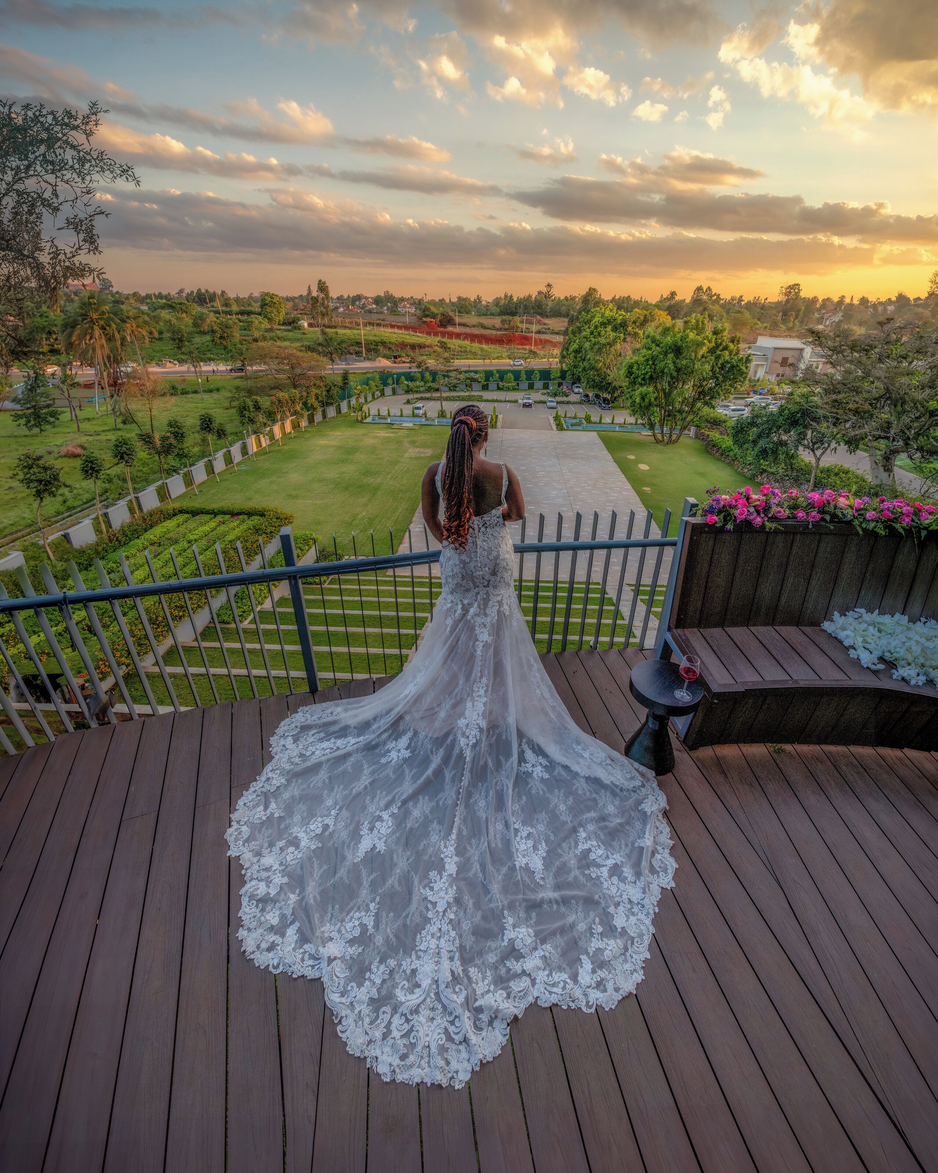 Una mujer con vestido de novia blanco en una cubierta de madera con vistas a un jardín ajardinado y una zona residencial.