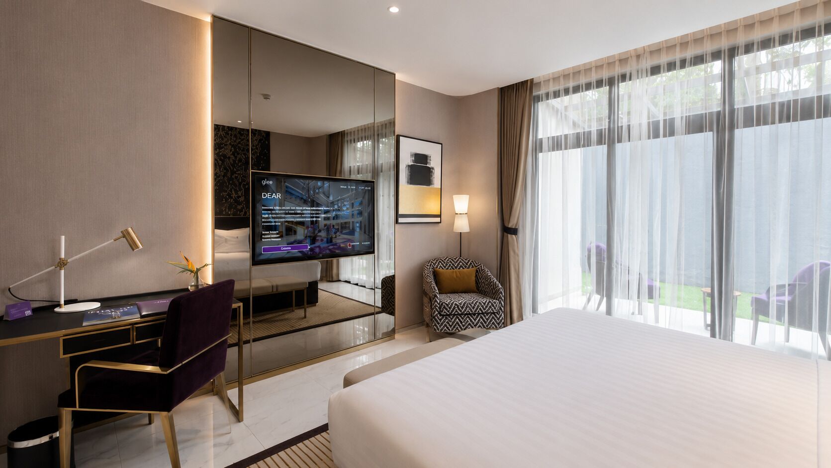 A hotel room with a bed, desk, chair, TV, and large windows.