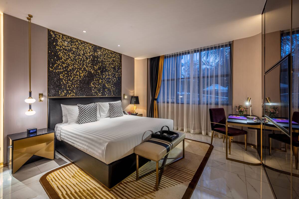 A modern hotel room with a large bed, bedside tables, a desk, and a view of the outdoors.