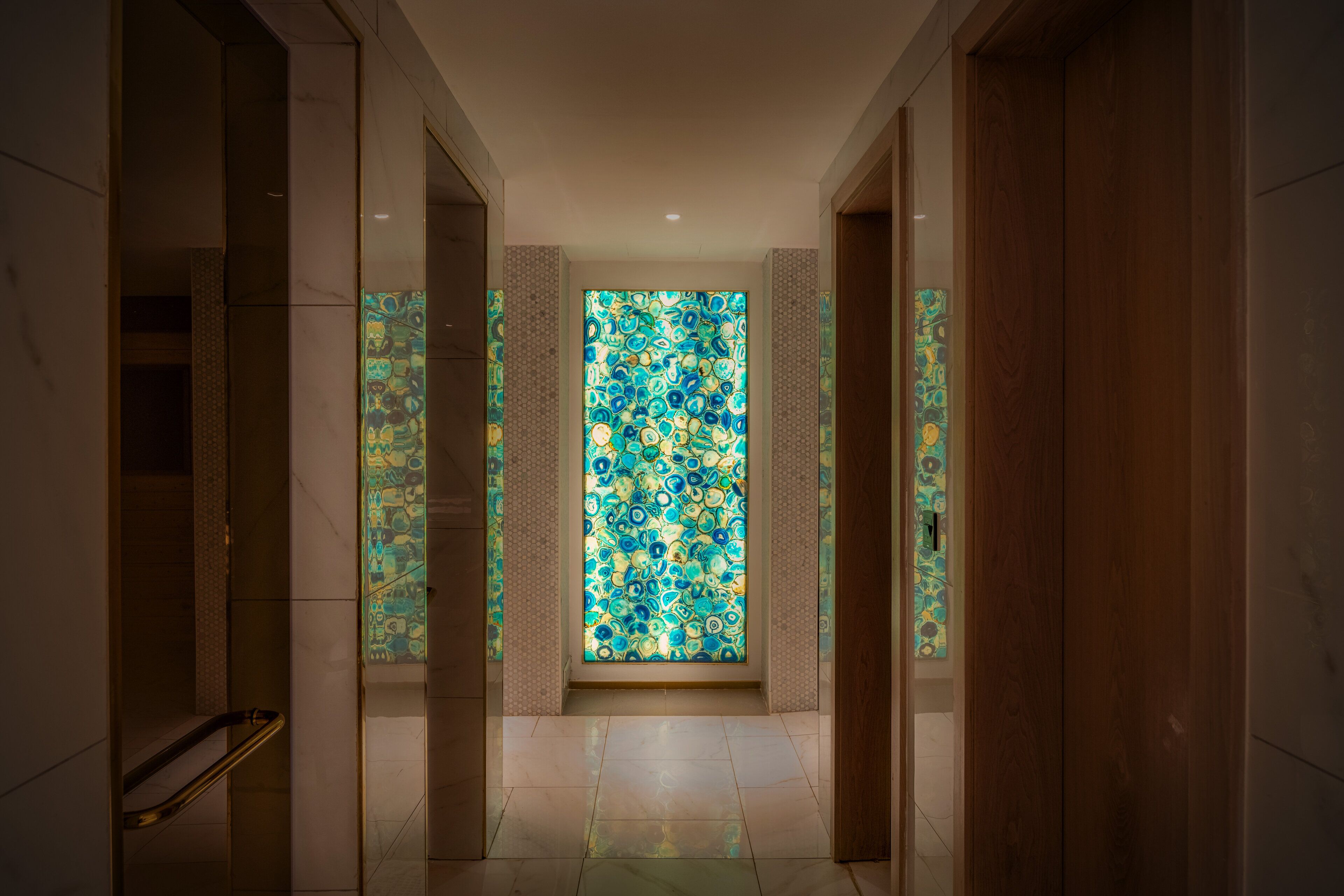 A hallway with a large stained glass window, marble walls, and a wooden door.