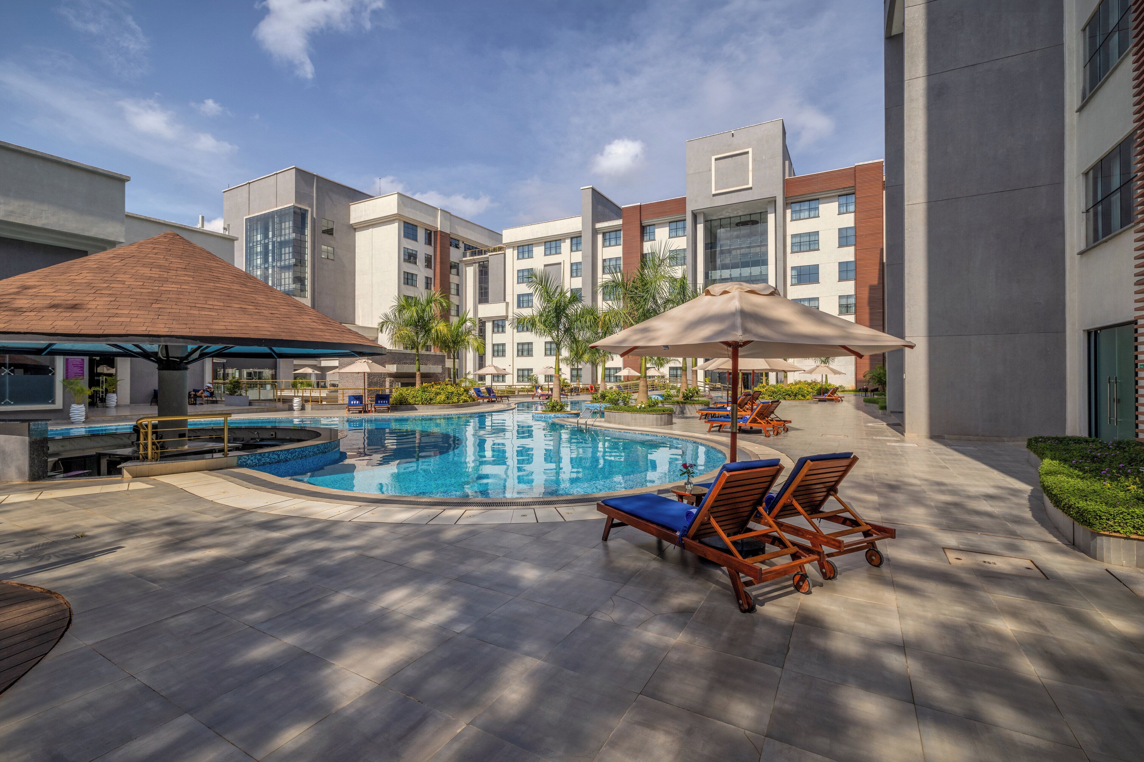 A modern hotel courtyard with a swimming pool, sun loungers, and a covered seating area.
