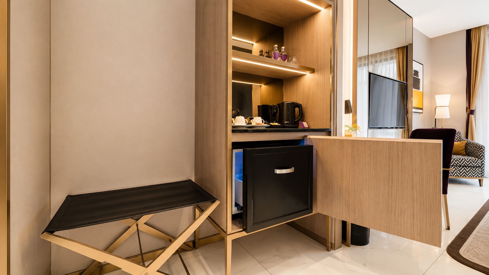 A compact hotel room with a kitchenette, a small desk, and a seating area with a sofa.