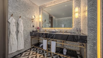 Un baño moderno con suelo de baldosas blanco y negro, un espejo grande y dos albornoces blancos colgados en un perchero.