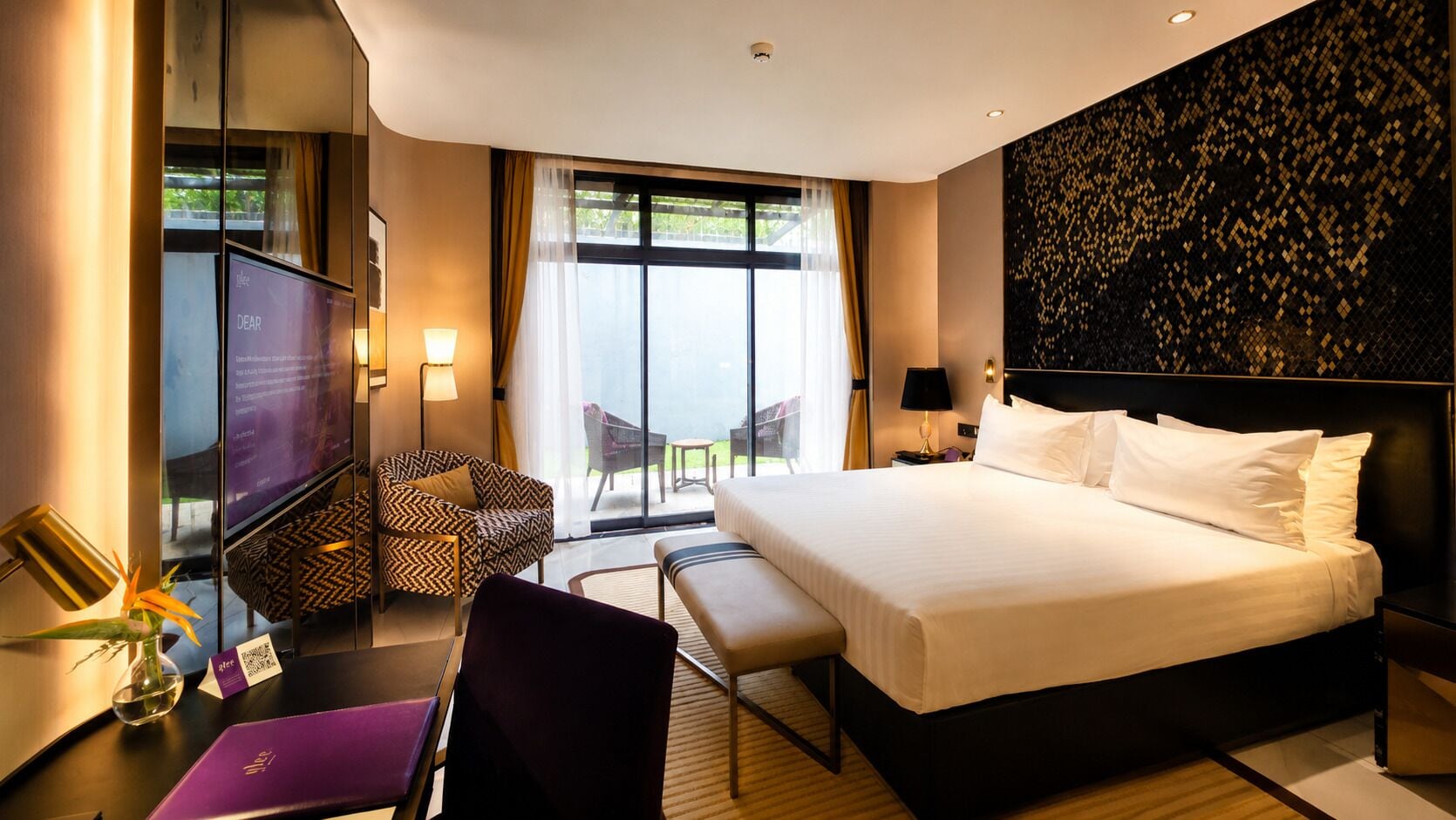 Habitación de hotel con una cama grande, un escritorio con una computadora, una silla, un televisor y vistas al exterior.