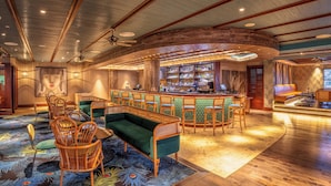 Un salón amplio con zona de bar, suelo de madera y un tapiz decorativo grande.