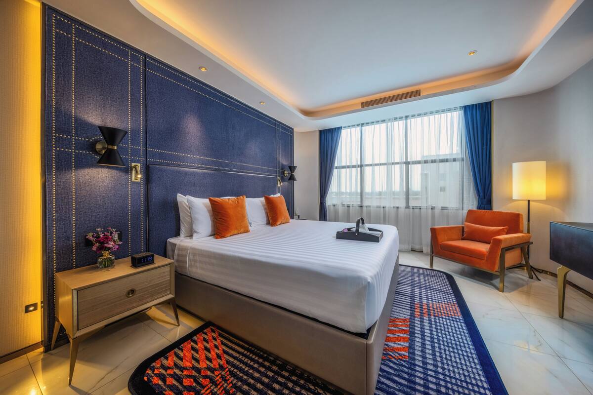 A modern hotel room with a large bed, a bedside table, a chair, and a TV.