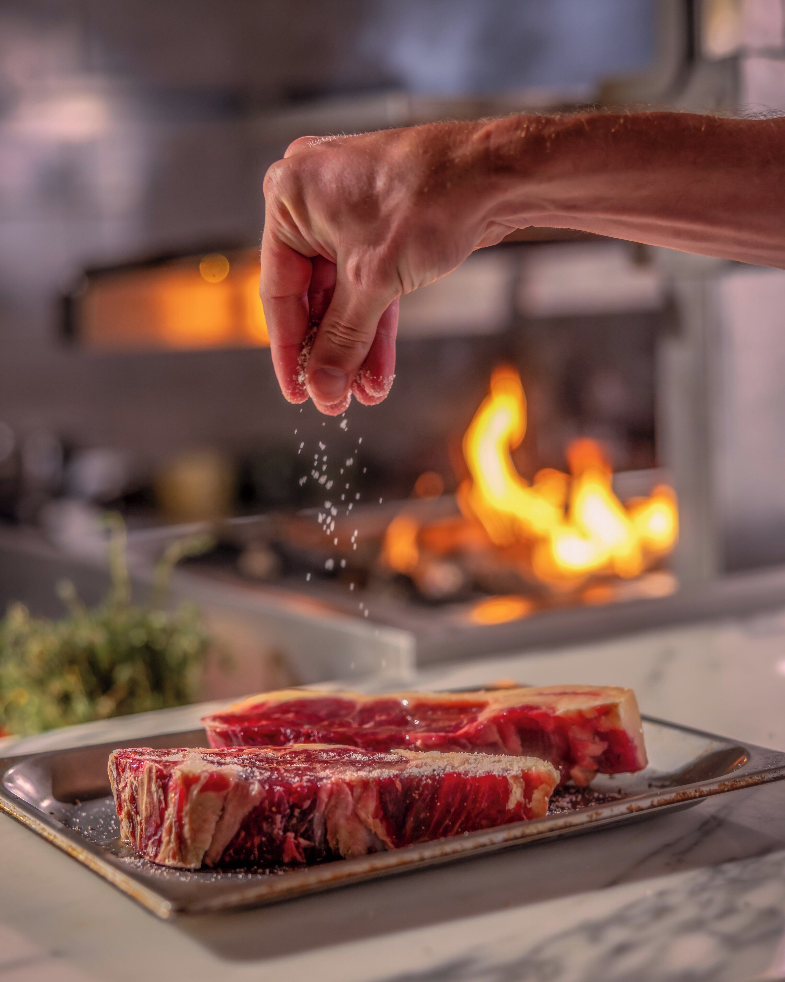 A hand sprinkling seasoning over a steak on a plate.