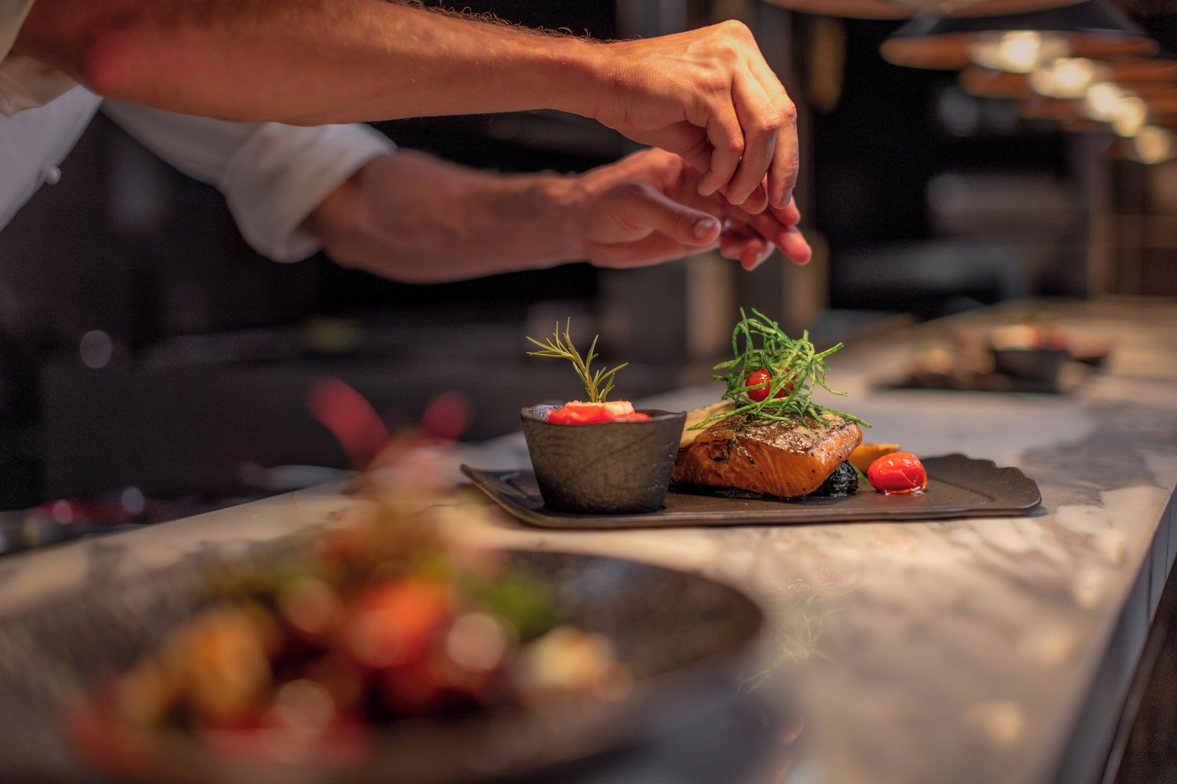 A chef's hands preparing a dish with salmon and vegetables on a plate.