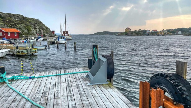 Een houten steiger met boten, een vuurtoren en huizen aan het water.