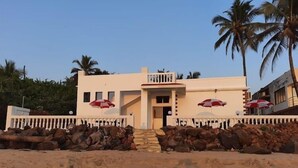 A two-story building with a balcony, a stone wall in front, and palm trees in the background. - White Seasons Resort And Spa (Malvan)