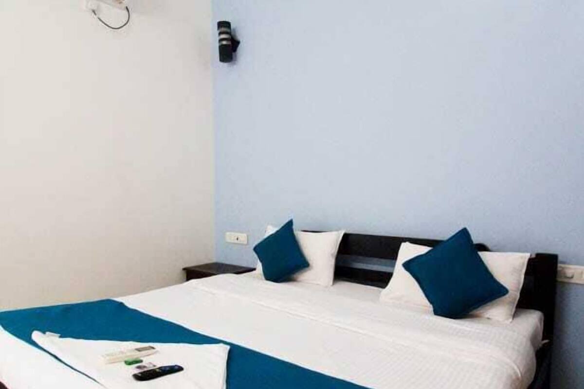 A neatly made bed with a white and blue bedspread, a black headboard, and two blue pillows.