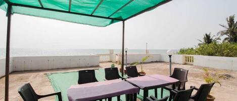 A covered outdoor seating area with tables and chairs, overlooking a beach.