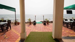 A covered outdoor seating area with tables and chairs, a view of the sea, and potted plants. - White Seasons Resort And Spa (Malvan)