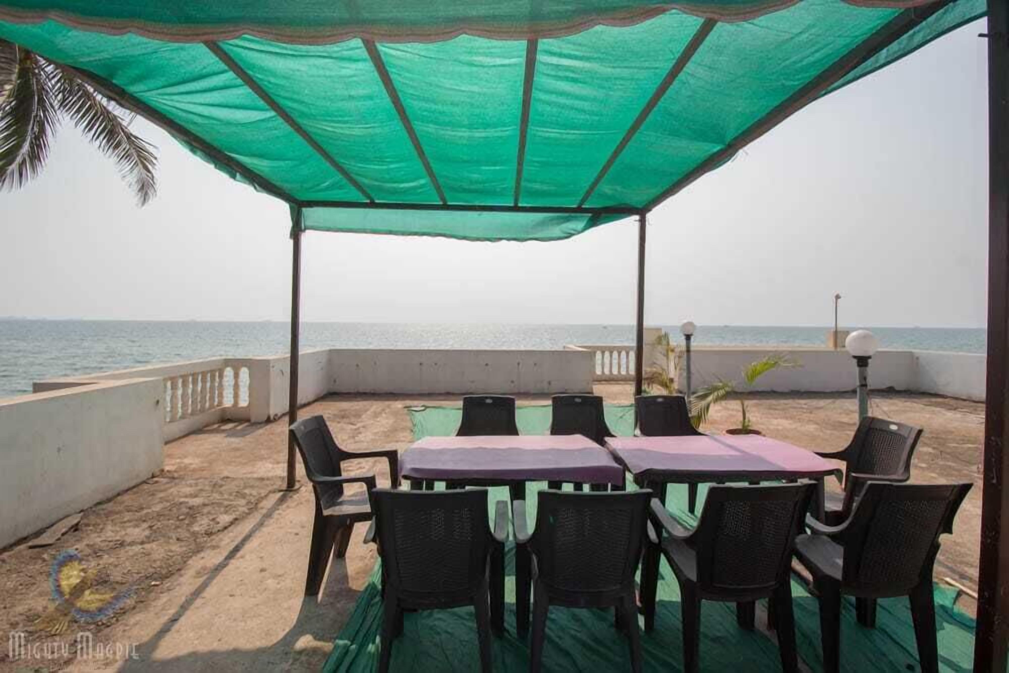 Un área de estar al aire libre, techada, con una mesa y sillas, con vista al mar.