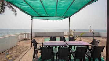 Un área de estar al aire libre, techada, con una mesa y sillas, con vista al mar.