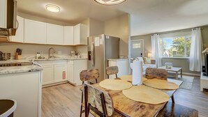 A modern kitchen with white cabinets, a wooden dining table with woven placemats, and a view of the living area through a large window. - TJ Maxx (Colorado Springs)