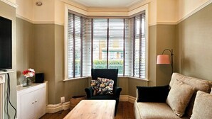 Une chambre d’angle avec une baie vitrée, une télévision, une table, une chaise et un canapé.