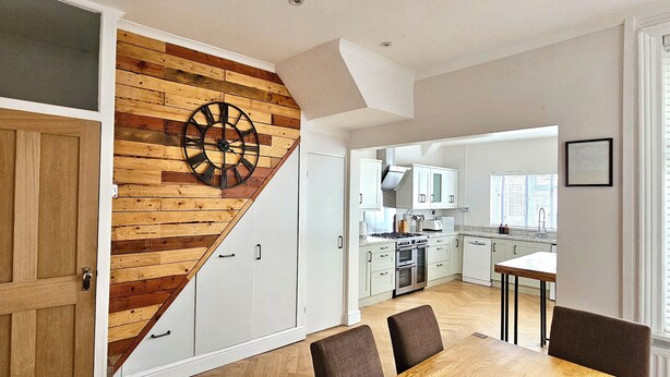 Une cuisine moderne avec des armoires blanches, un mur d’accent en bois et une grande horloge.