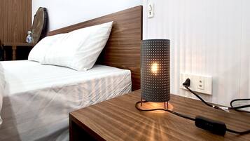 Una cama bien hecha con sábanas blancas, un cabecero de madera y una mesita de noche con una lámpara.
