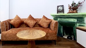 A living room with a brown sofa, a round wooden coffee table, a green fireplace, and a framed picture on the mantel. - Amelie Homestay (Hanoi)