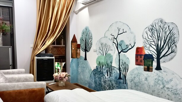 A hotel room with two beds, a desk with a computer, a wall mural of trees and houses, and a window with curtains. - Amelie Homestay (Hanoi)