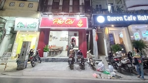 A street view at night with a restaurant named "Pho Cai" and a hotel named "Queen Cafe Hotel". - Amelie Homestay (Hanoi)