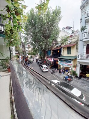 A street view with buildings, a tree, and a white car. - Amelie Homestay (Hanoi)