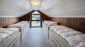 Una habitació de dormitori amb dos llits, parets de fusta, sostre inclinat i una finestra gran.