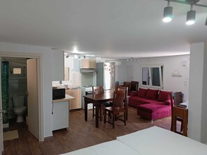 A compact living space with a kitchenette, dining area, and a sofa. - Thor & Freyja's of Poseidonia Syros Holiday House (Syros)