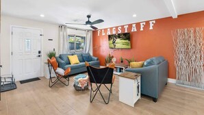 A modern living room with a sofa, armchair, and a small table. A ceiling fan is visible, and the room has a large window. - 5BR/3BA Mountain Retreat: Fun in Flagstaff (Flagstaff)