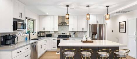 Una cocina moderna con armarios blancos, electrodomésticos de acero inoxidable y una isla central con taburetes de bar.