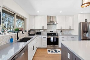 Una cocina moderna con armarios blancos, electrodomésticos de acero inoxidable y un ventanal amplio.