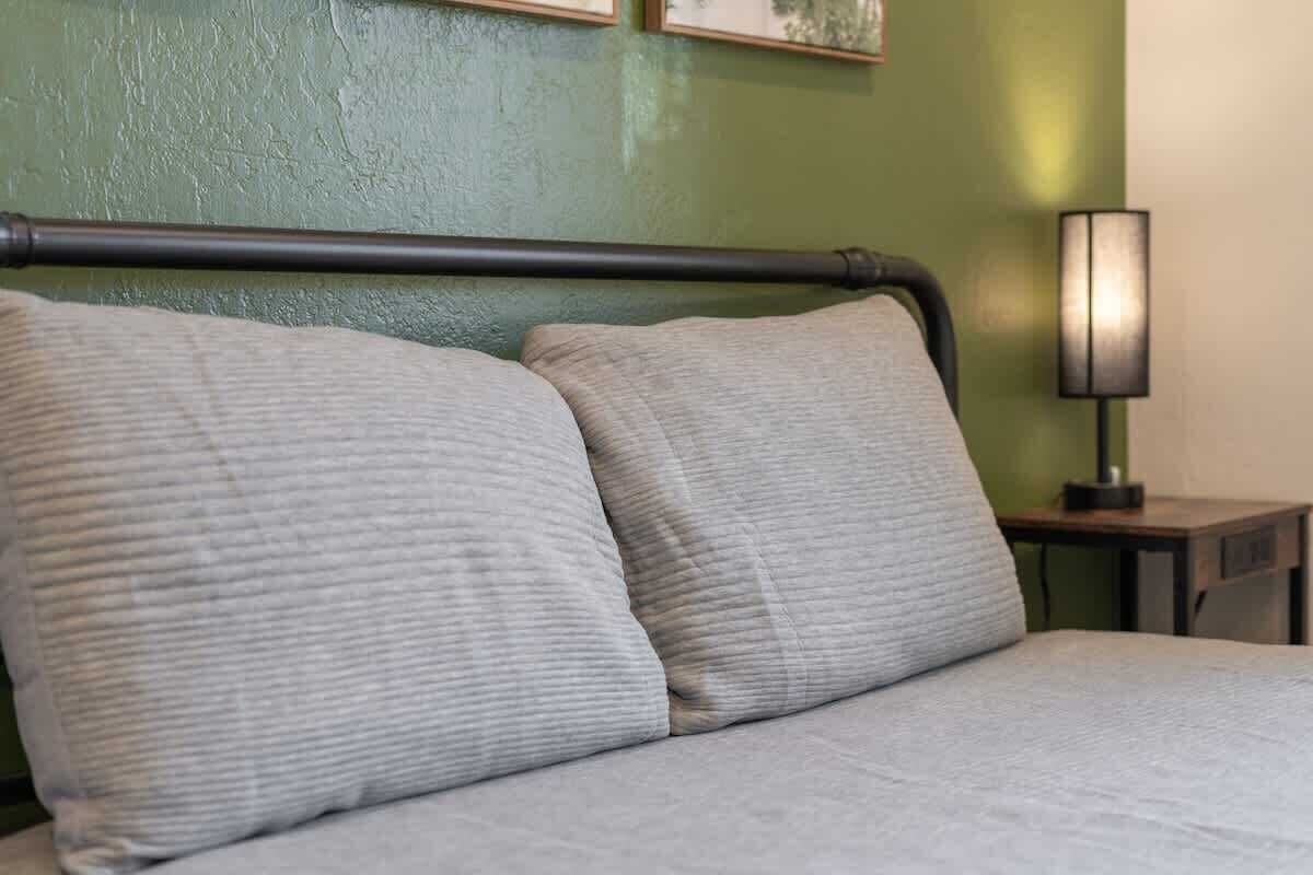 Una cama con cabecera, dos almohadas y una mesita de noche con lámpara.