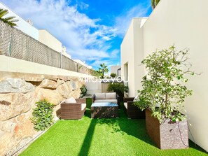 Une terrasse extérieure moderne, dotée d’un gazon synthétique, de murs en pierre et de meubles en osier.