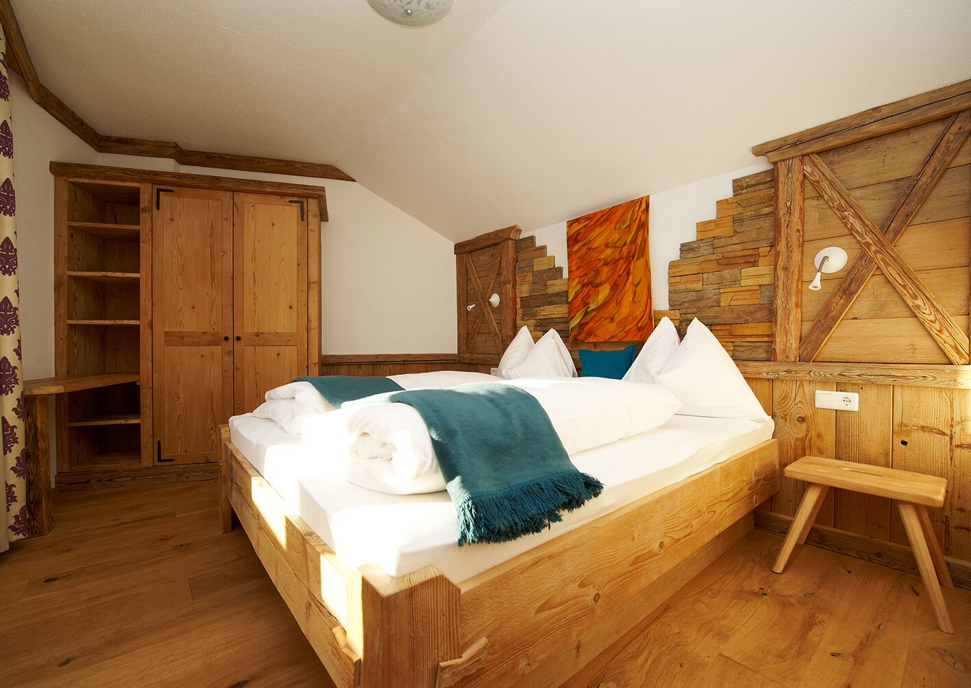 Un lit en bois avec du linge de lit blanc et un plaid turquoise, une armoire en bois et un mur en pierre avec un plafond en bois.