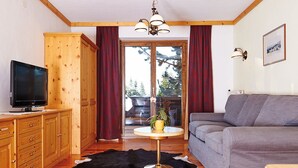 Una sala de estar acogedora con un mueble de madera, un televisor de pantalla plana, un sofá gris, una mesa de centro redonda con una planta y un tapete de cuero negro y blanco.