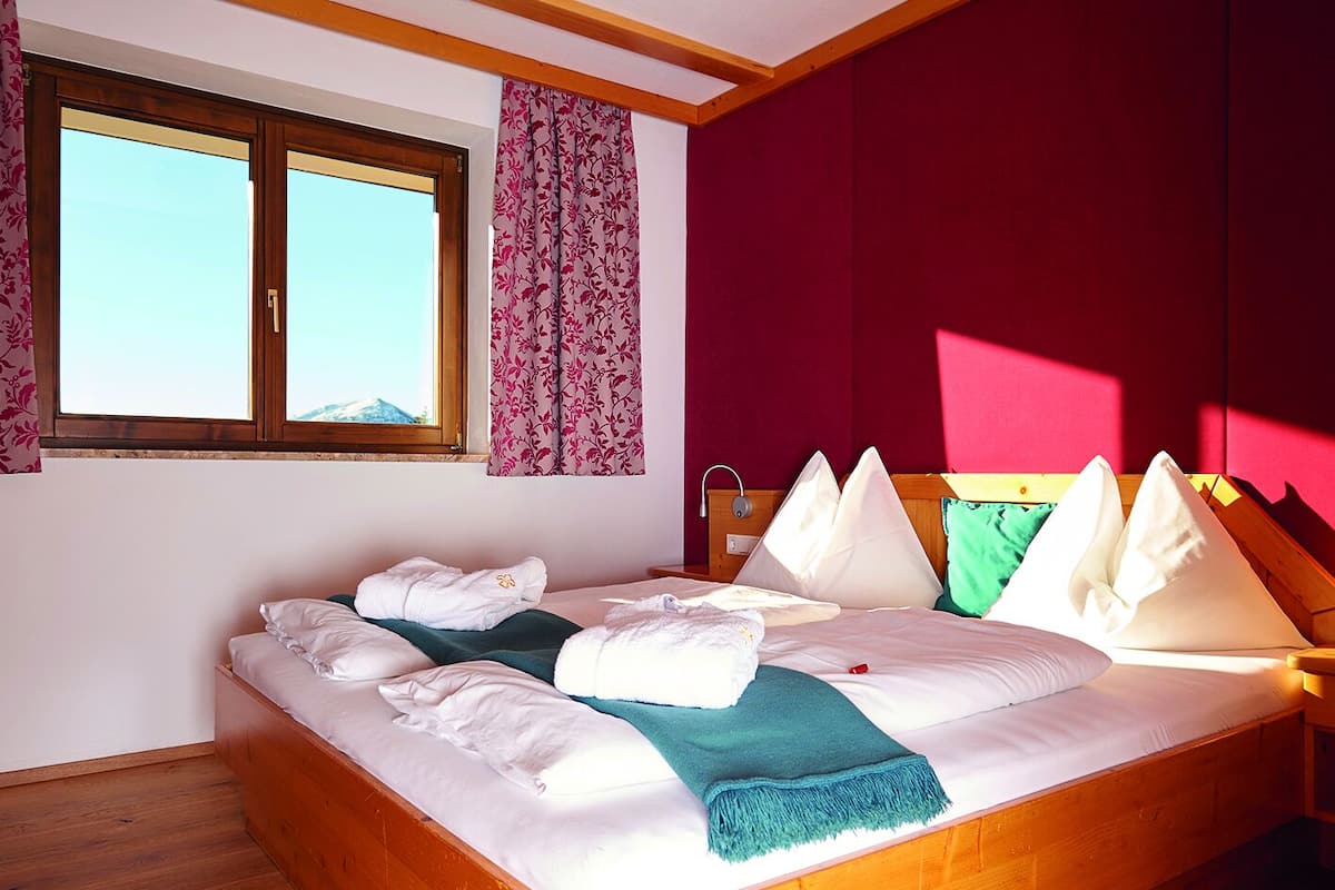 A bedroom with a wooden bed, white bedding, and a view of the sky through a window.