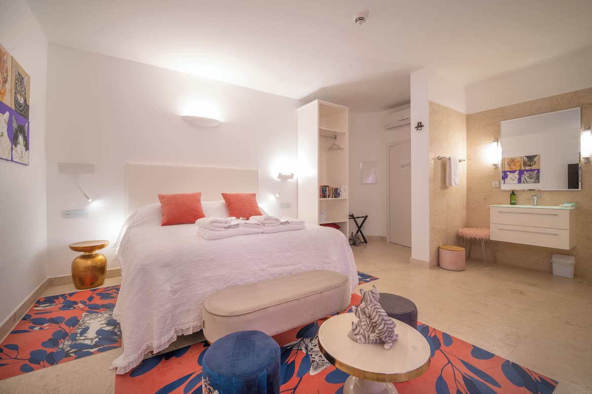 A modern bedroom with a bed, bedside table, bench, and a round table with a cat.