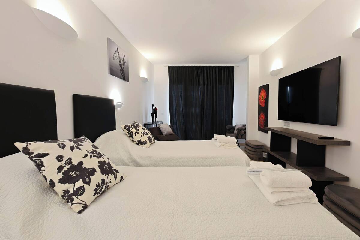 A hotel room with two beds, a TV, a desk, and a large window with curtains.