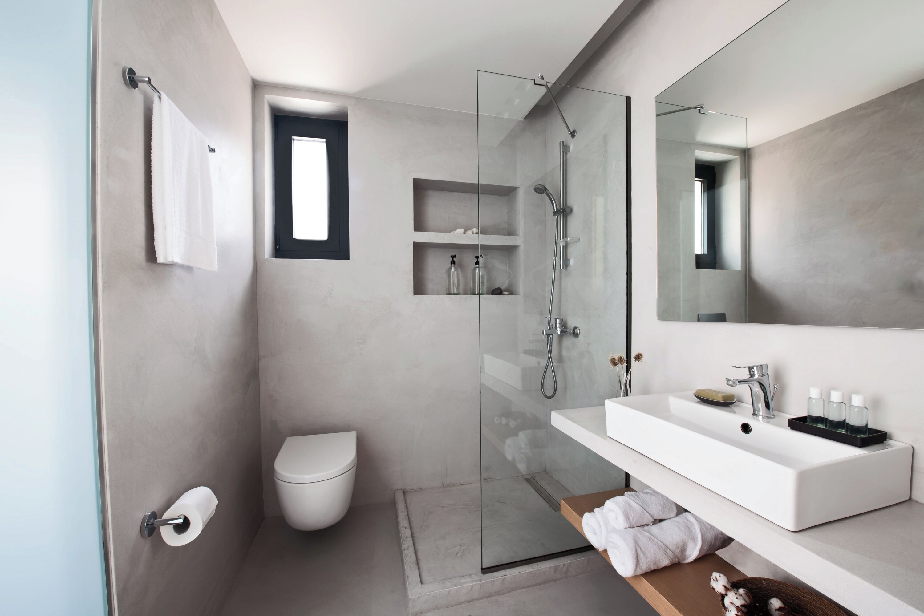 A modern bathroom with a glass shower enclosure, a white toilet, and a large mirror above a white sink with toiletries.
