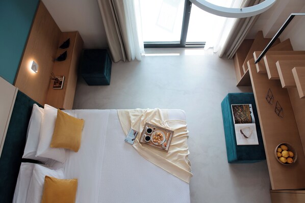 A modern hotel room with a bed, a small table with a tray of food, a bowl of fruit, and a window with curtains. - Chronos Hotel (Sithonia)