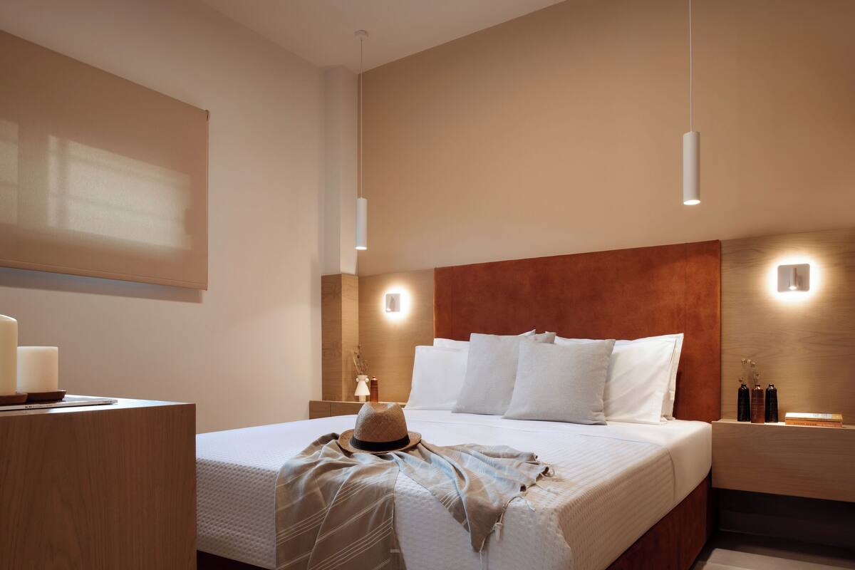 A modern hotel room with a large bed, a wooden nightstand, a desk, and a wall-mounted TV.