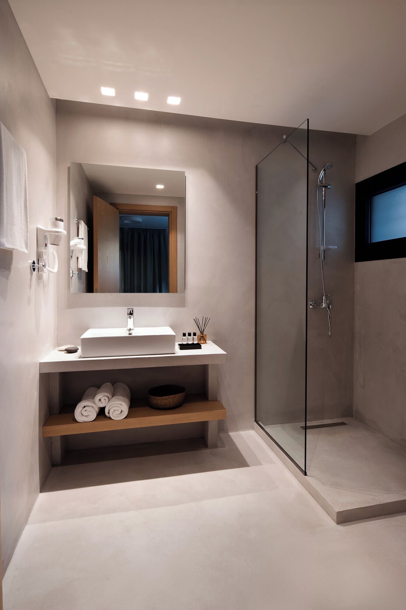 Een moderne badkamer met een glazen douchecabine, een witte wastafel met spiegel erboven en keurig opgevouwen handdoeken op een plank.