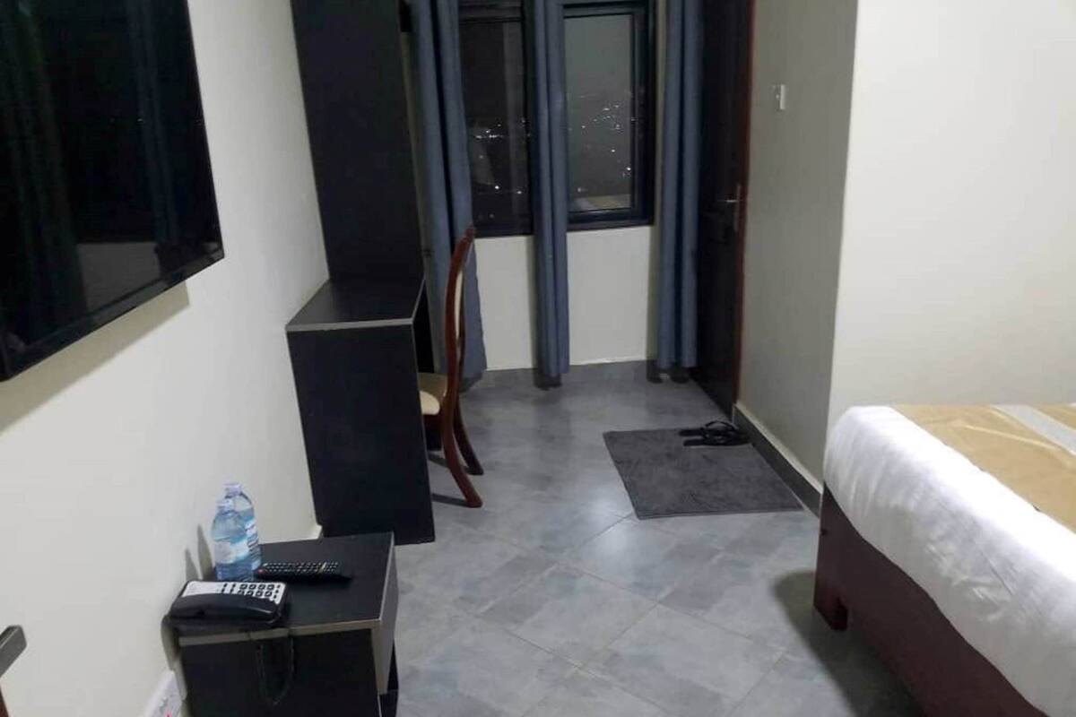 Habitación de hotel con cama, escritorio con silla, televisor montado en la pared y ventana con cortinas.