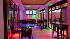 Un espacio interior moderno con mesas y sillas, ventanas amplias e iluminación empotrada en el techo.