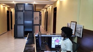 Zona de recepción con un separador de vidrio, un mostrador con computadora y una persona de pie.